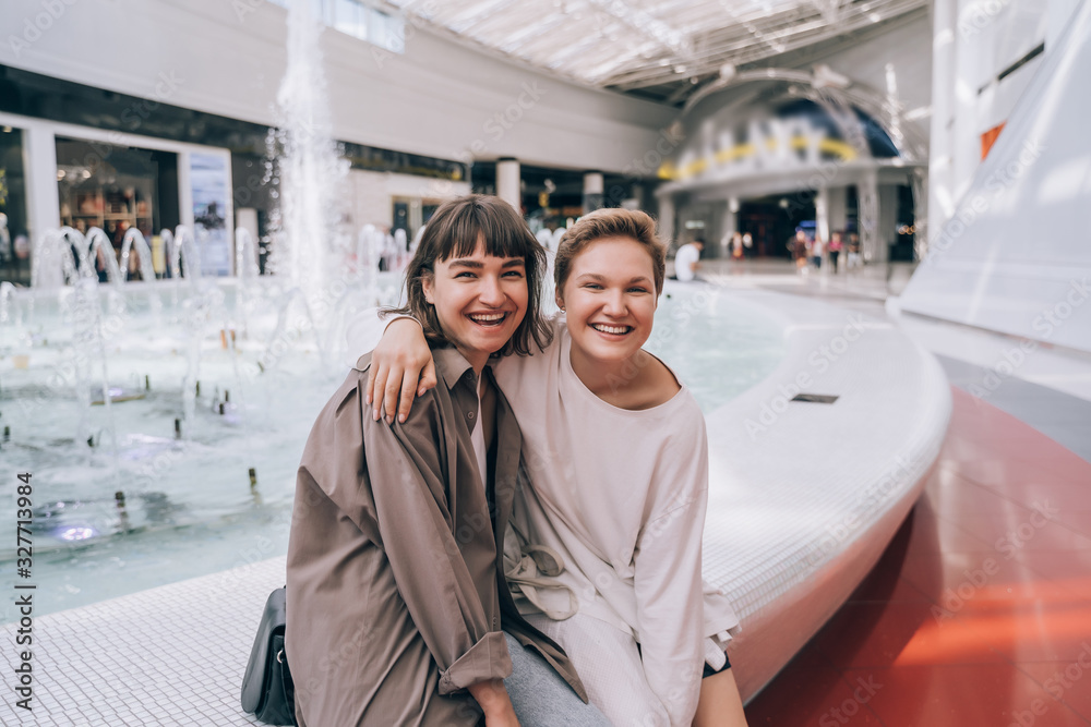 Two girls have fun in the mall, a fountain in the background Two girls have fun in the mall, a fountain in the background