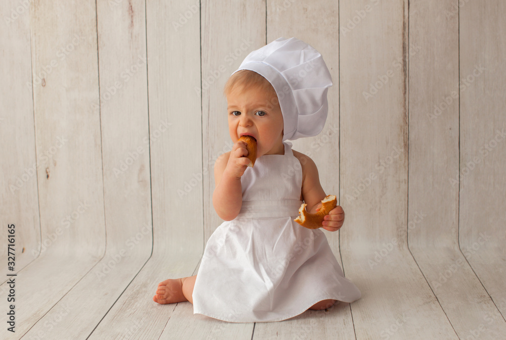 Cute ten months old baby boy, in a suit of a cook, sits on a light wooden background. Chef's hat on his head. He is a bakery cook. Cute ten months old baby boy, in a suit of a cook, sits on a light wooden background. Chef's hat on his head. He is a bakery cook.