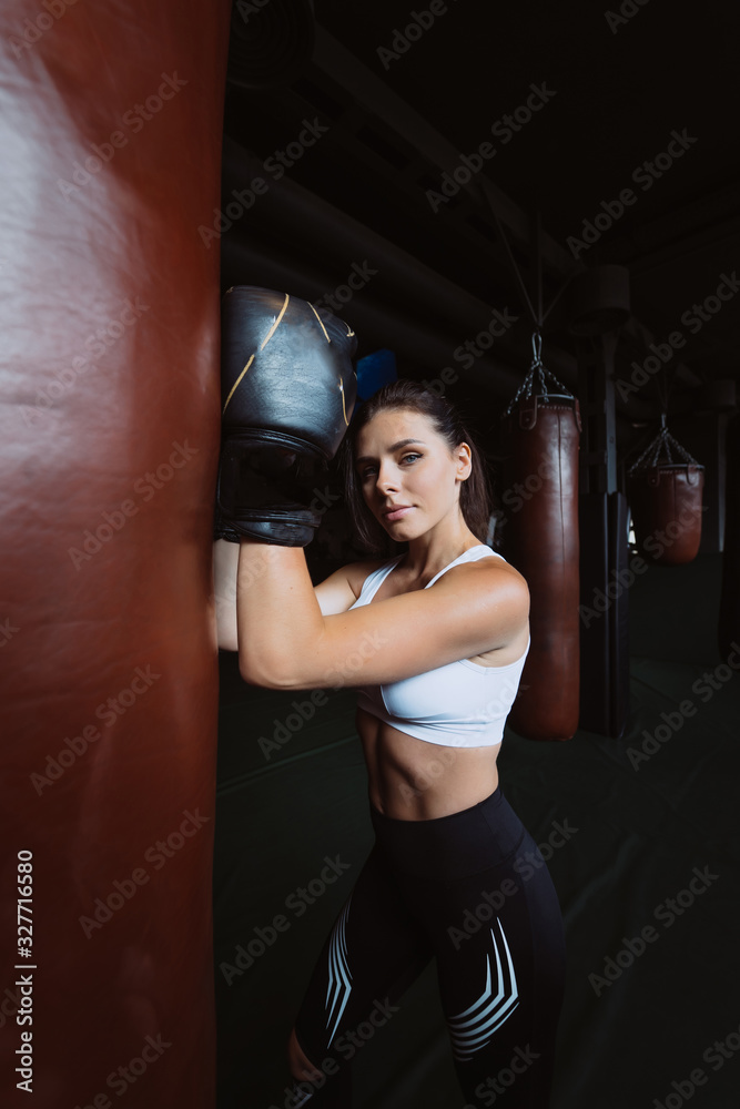 Boxing woman posing with punching bag, on dark background. Strong and independent woman concept