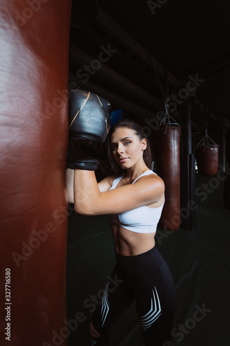 Boxing woman posing with punching bag, on dark background. Strong and independent woman concept © teksomolika
