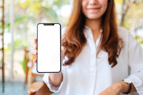 Mockup image of a beautiful woman holding and showing mobile phone with blank white screen in cafe photo