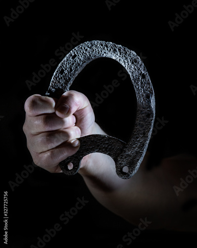 A man holds an old, rusty horseshoe against a black background in his hand. Concept: talisman and luck