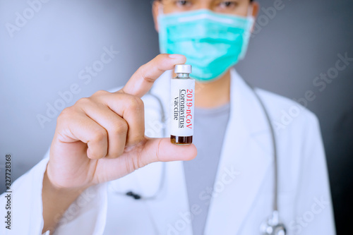 Hand of doctor holding coronavirus vaccine bottle with grey background photo