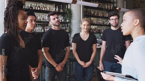 Female restaurant bar manager with digital tablet giving motivational talk to waiting staff before opening - shot in slow motion