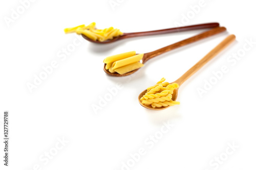 Various types of italian pasta concept. Raw gemelli, penne, casarecce in wooden spoons on white background. Copy space.