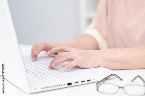 Close up hands of elderly person work on laptop computer in a office © Ermolaev Alexandr