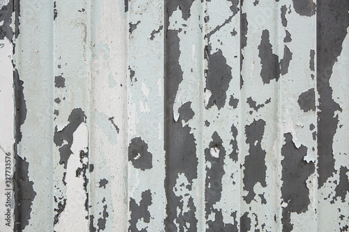 Old shabby metal sheet fence texture. Pattern of old metal sheet. Background of iron fence with peeled pieces of old cracked light paint layer.