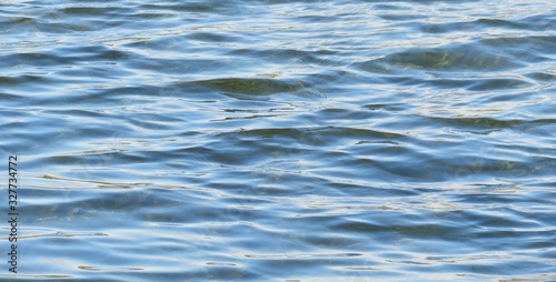 Ripples on light blue water, sun glare on river water texture 