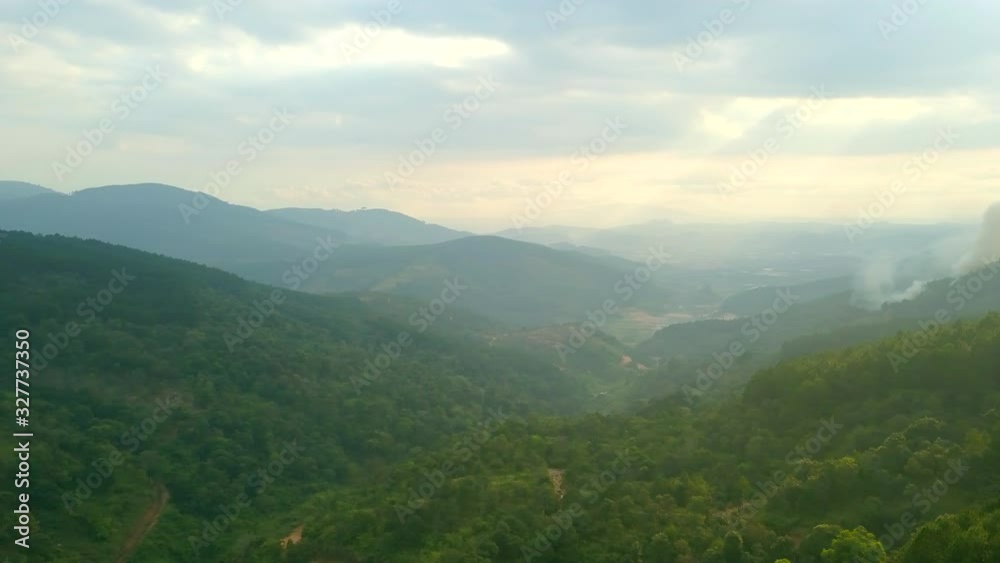 Drone shot of the sun shining through clouds with beautiful sun rays showing over hills of Dalat, Vietnam in Asia. Green forest and mountains and village. Drone shot of the sun shining through clouds with beautiful sun rays showing over hills of Dalat, Vietnam in Asia. Green forest and mountains and village.