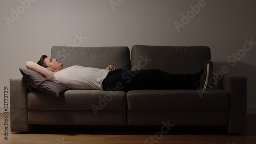 Sad alone young adult man lies on a sofa in the night