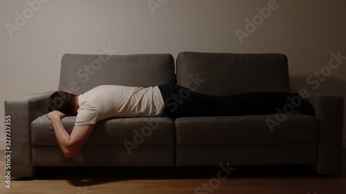Young adult man in a white t-shirt and jeans lies on sofa in the night