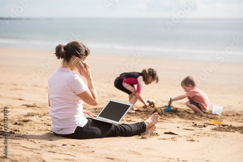 Woman attending phone call as kids go busy on the beach © Martinan