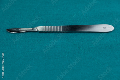 Surgical instrument, stainless steel scalpel handle number 3 with blade number 10 isolated on surgical green drape fabric.