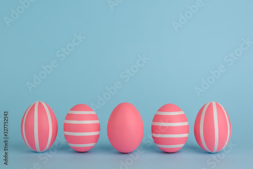 Easter decorated pink eggs. Five striped pink eggs in a row on a blue background. Isolated. White stripes. Colourful Easter concept. Copy space. Happy Easter card.