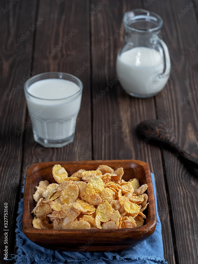 Jug and glass of milk , corn cereals in a wooden plate on dark wooden table. Close up. Shallow depth of field. Jug and glass of milk , corn cereals in a wooden plate on dark wooden table. Close up. Shallow depth of field.