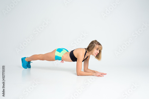 Concentrated beautiful fitness girl in sportwear exercising doing a plank over white background. Copyspace