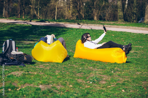 couple laying on yellow inflatable mattress in city park. reading book. taking selfie © phpetrunina14