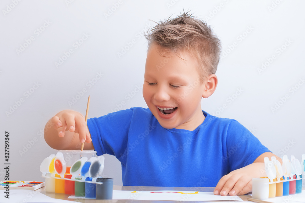 Laughing cheerful boy of seven years with messy hair holds a brush in his hands and draws with colorful paints Laughing cheerful boy of seven years with messy hair holds a brush in his hands and draws with colorful paints