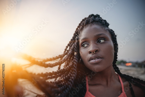 Charming beautiful young african american woman girl with black pigtails with piercings on her face on the beach at sunset.
