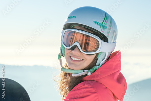 Portrait of a sportswoman wearing helmet and mask with snowboard in hand looking at camera