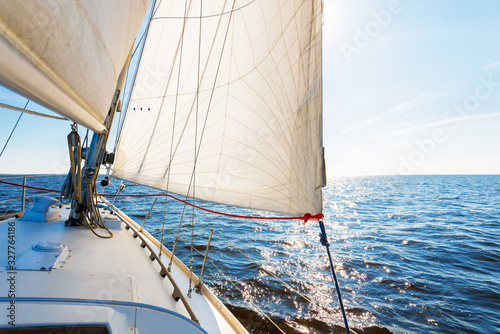 White sloop rigged yacht sailing in an open Baltic sea on a clear sunny day. A view from the deck to the bow, mast and sails. Waves and water splashes. Estonia photo