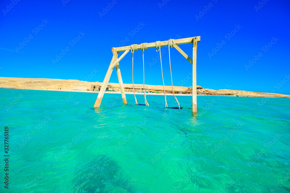Swing in crystal clear azure water - Orange Bay Beach with white beach - paradise coastline of Giftun island, Mahmya, Hurghada, Red Sea, Egypt Swing in crystal clear azure water - Orange Bay Beach with white beach - paradise coastline of Giftun island, Mahmya, Hurghada, Red Sea, Egypt