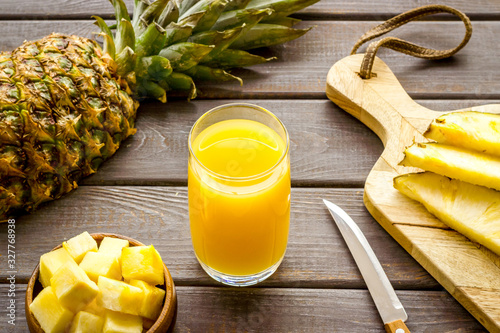Bild auf Leinwand Pineapple juice in glass closeup near sliced fruit on wooden background
