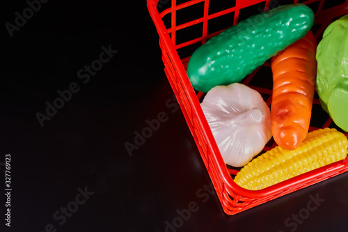 Fototapeta Plastic vegetables lie in a red plastic basket on a dark background.