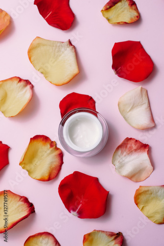 Open moisturizer on a pink pastel background among red, orange rose petals. The concept of skin care, anti-aging care, natural ingredients in cosmetics