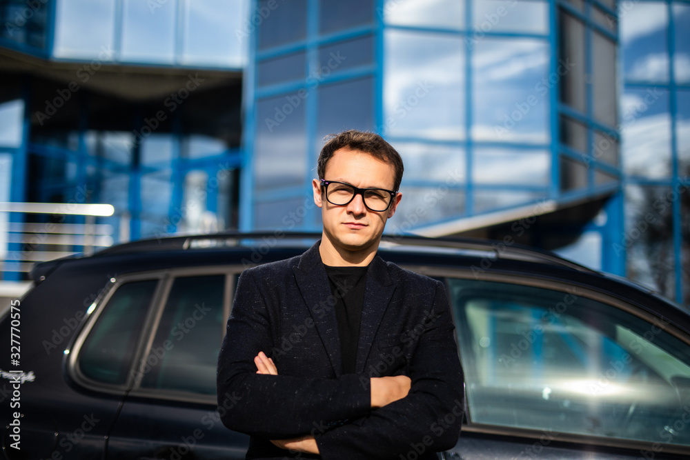 Smiling business man standing next to his car on scyscraper background
