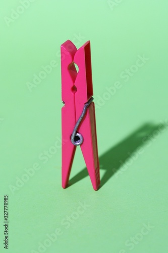 pink colored plastic clothespin on green background. Minimal concept art. Abstraction. Shadows. Color clothes-peg isolated.