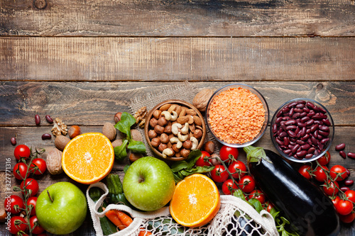 Concept of healthy vegan food, clean eating. On wooden background: vegetables, fruits, nuts, beans, lentils. Ripe seasonal product for clean meal. Copy space, flat lay, top view