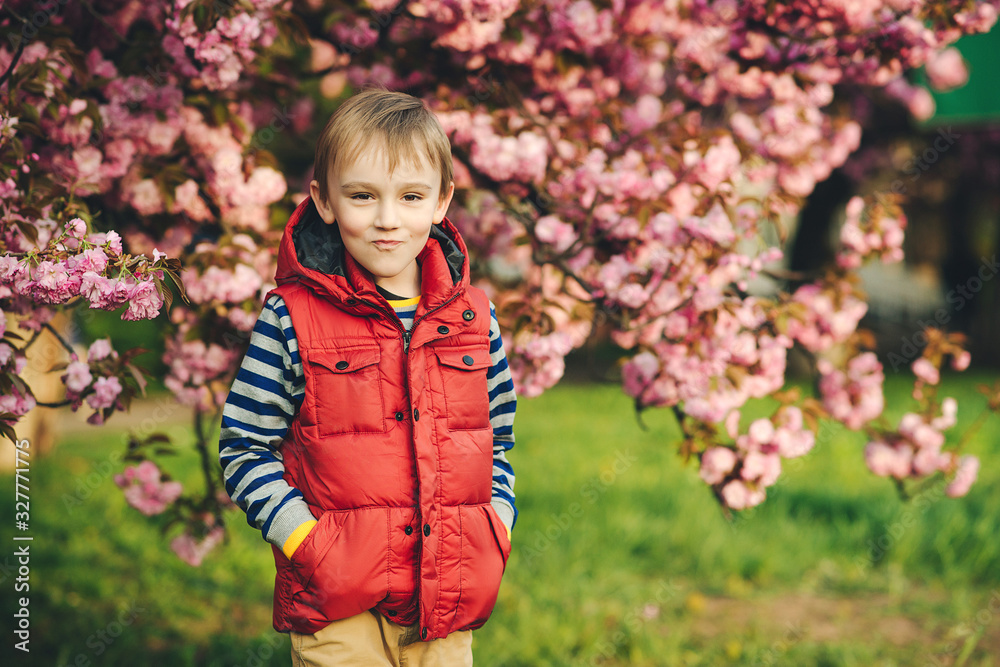 Fashionable kid in spring park. Kids emotioons and expression. Fashion, lifestyle and spring. Handsome stylish boy posing over sakura blooming