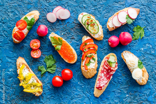 Sandwiches - set with vegetables, caviar, salami - on blue background top-down