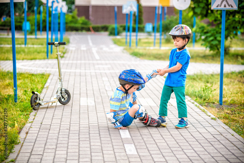 two boys in park, help boy with roller skates to stand up