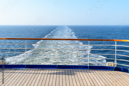 Aft deck of a wooden-coated cruise ship with railings. View of the wake waves behind the stern. Sea horizon in the ocean.