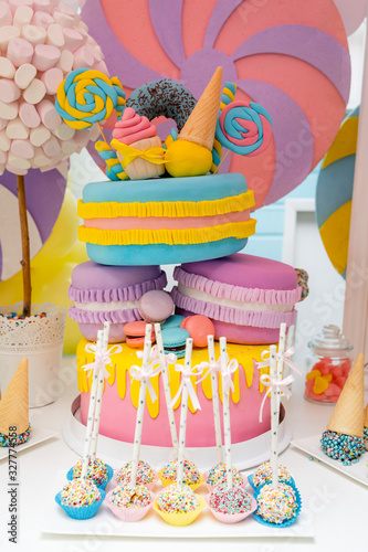 Bar with sweets and a three-story multi-colored cake with macarones. photo