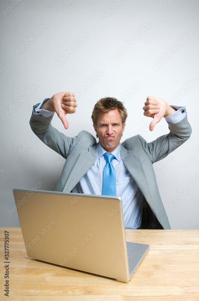 Office worker at his computer looking at the camera with a frown and two thumbs down Office worker at his computer looking at the camera with a frown and two thumbs down