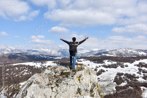 Tourist man is feeling free and standing with hands up on the top of the mountain. Climber enjoy in mountains in spring. Beautiful landscape