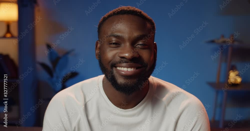 Portrait of cheerful young bearded man smiling and looking to camera. Close up view of handsome guy in good mood sitting and looking happy. Cosy home background. Portrait of cheerful young bearded man smiling and looking to camera. Close up view of handsome guy in good mood sitting and looking happy. Cosy home background.
