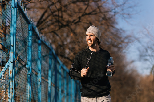 Happy male athlete with water bottle jogging outdoors.