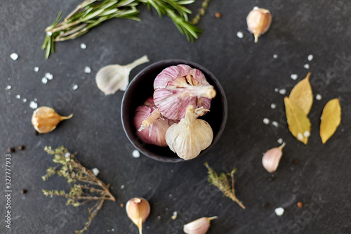 food, culinary and eating concept - garlic in bowl, rosemary and salt on stone surface