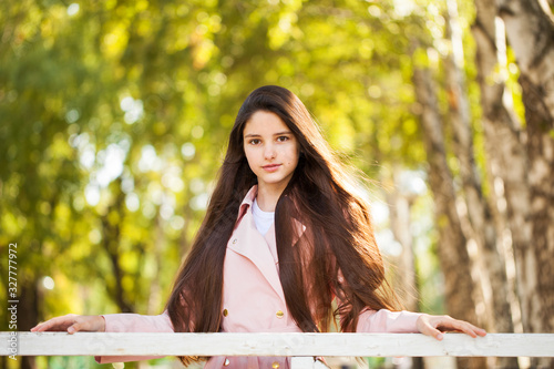 Portrait of a young brunette girl in pink coat on a background of autumn park photo