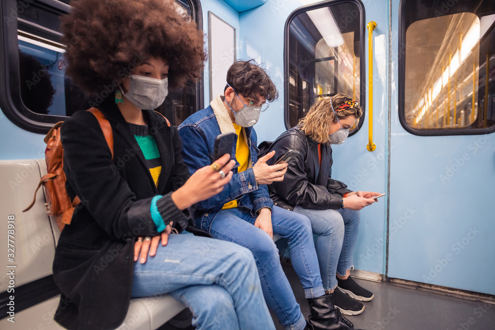 Three multiethnic friends wearing medical mask protecting from pollution and virus in the subway using smartphone