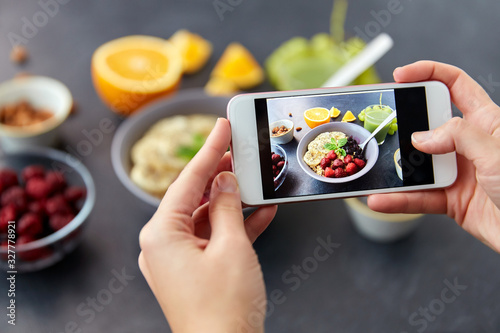 food, eating and breakfast concept - hand of woman taking picture of cereals in bowl with fruits, berries and juice with smartphone