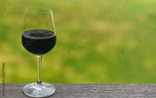 A glass of red wine on wooden table with blurry green background.