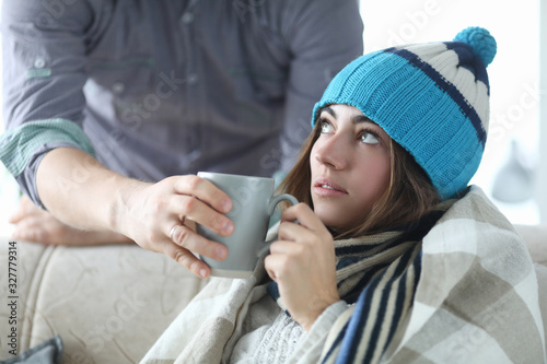Close-up of sick woman taking cup of tea with medication. Cute ill person in warm clothes looking away with calmness. Sickness and treatment concept