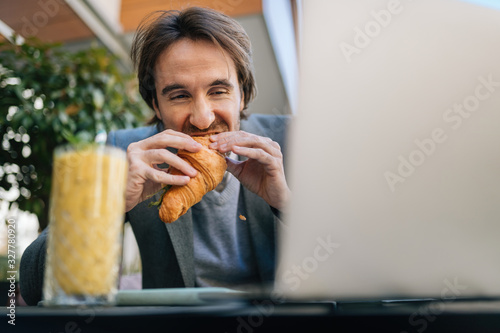 Hungry businessman eating croissant  on lunch break in a cafe 