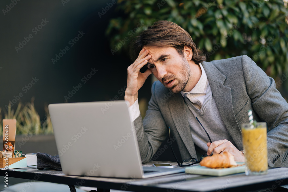 Pensive businessman reading problematic e-mail on laptop while sitting in cafe.