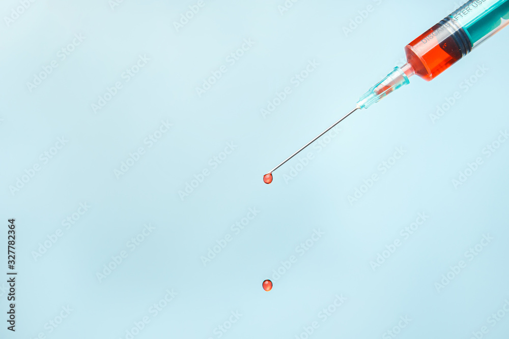 Syringe with a drop of blood at the end of the needle on a blue background. Syringe with a drop of blood at the end of the needle on a blue background.